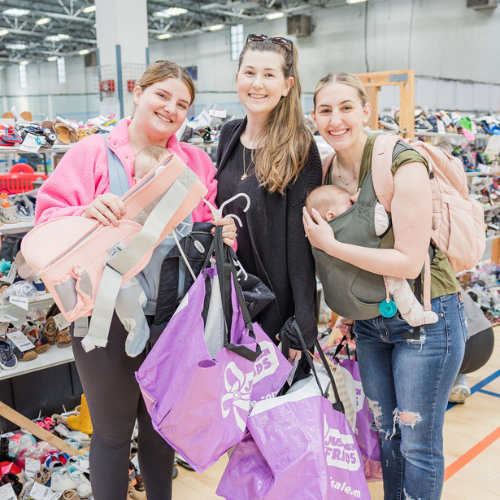 A mom and grandmother stand beside a rack of clothing at a JBF sale in Texas.